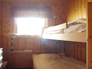 Un lit superposé avec une fenêtre au-dessus, un bureau avec une lampe et un mur en bois.
