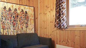 A room with a wooden paneled wall, a large abstract painting, a grey sofa, and a window with patterned curtains.