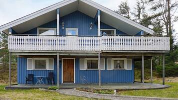Una casa azul de dos pisos con un balcón, una puerta de madera y un pequeño patio con sillas.