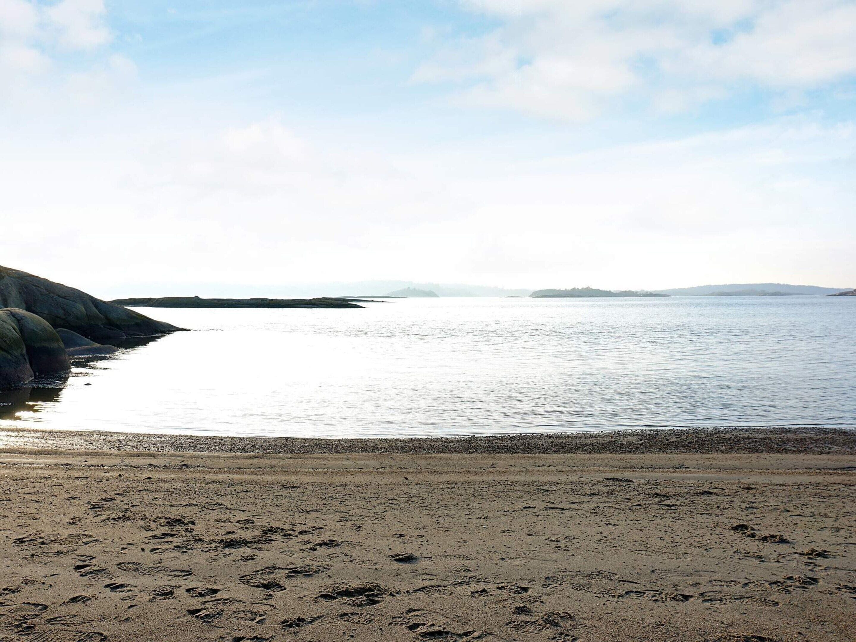 A beach with footprints in the sand, a calm sea, and a clear sky.