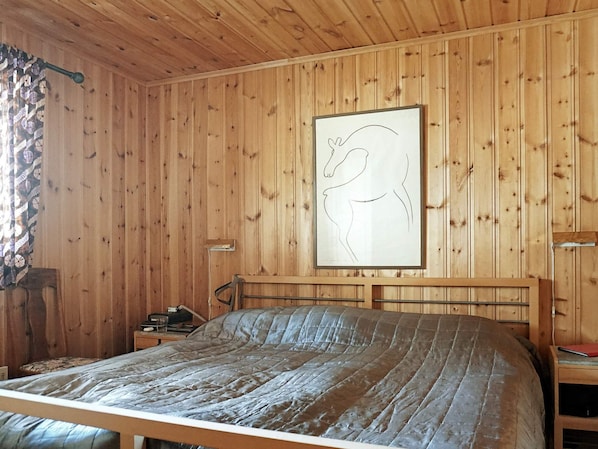 A wooden-paneled room with a bed, a nightstand, a wall-mounted picture, and a window with curtains.