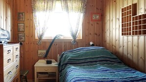 Une pièce en bois comprenant un lit, une commode, un bureau, une lampe et une fenêtre avec des rideaux.