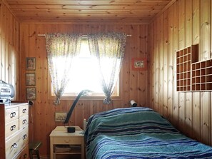 Une pièce en bois comprenant un lit, une commode, un bureau, une lampe et une fenêtre avec des rideaux.