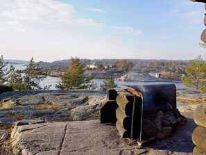 Un barbecue en pierre offrant une vue sur un lac et des bâtiments situés au loin.