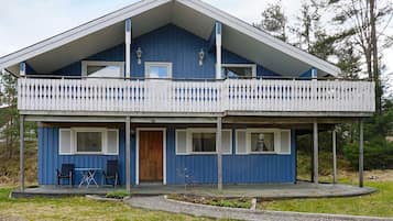 A two-story blue house with a balcony, a wooden door, and a small patio area.