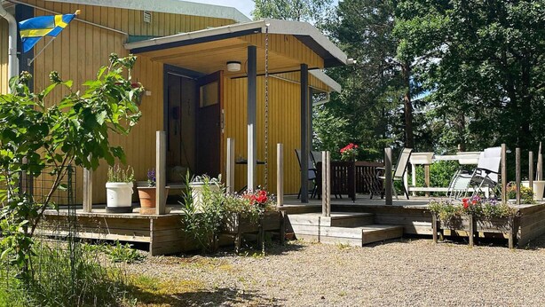 A wooden building with a covered porch, outdoor seating, and potted plants. - 6 Person Holiday Home in Bottnaryd (Bottnaryd)