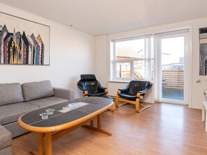 A living room with a grey sofa, a wooden coffee table, two leather chairs, and a large window with a view of a building outside. - 4 Person Holiday Home in Ansager (Ansager)