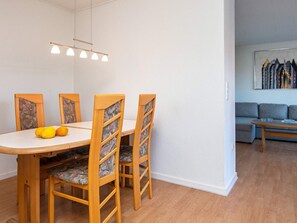 A dining area with a wooden table and chairs, a hanging light fixture, and a sofa in the background.