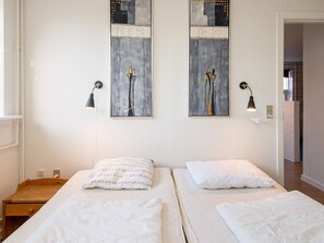 Hotellihuone, jossa on kaksi sänkyä, puinen yöpöytä, seinään kiinnitetty lamppu ja kehystetty abstrakti maalaus.