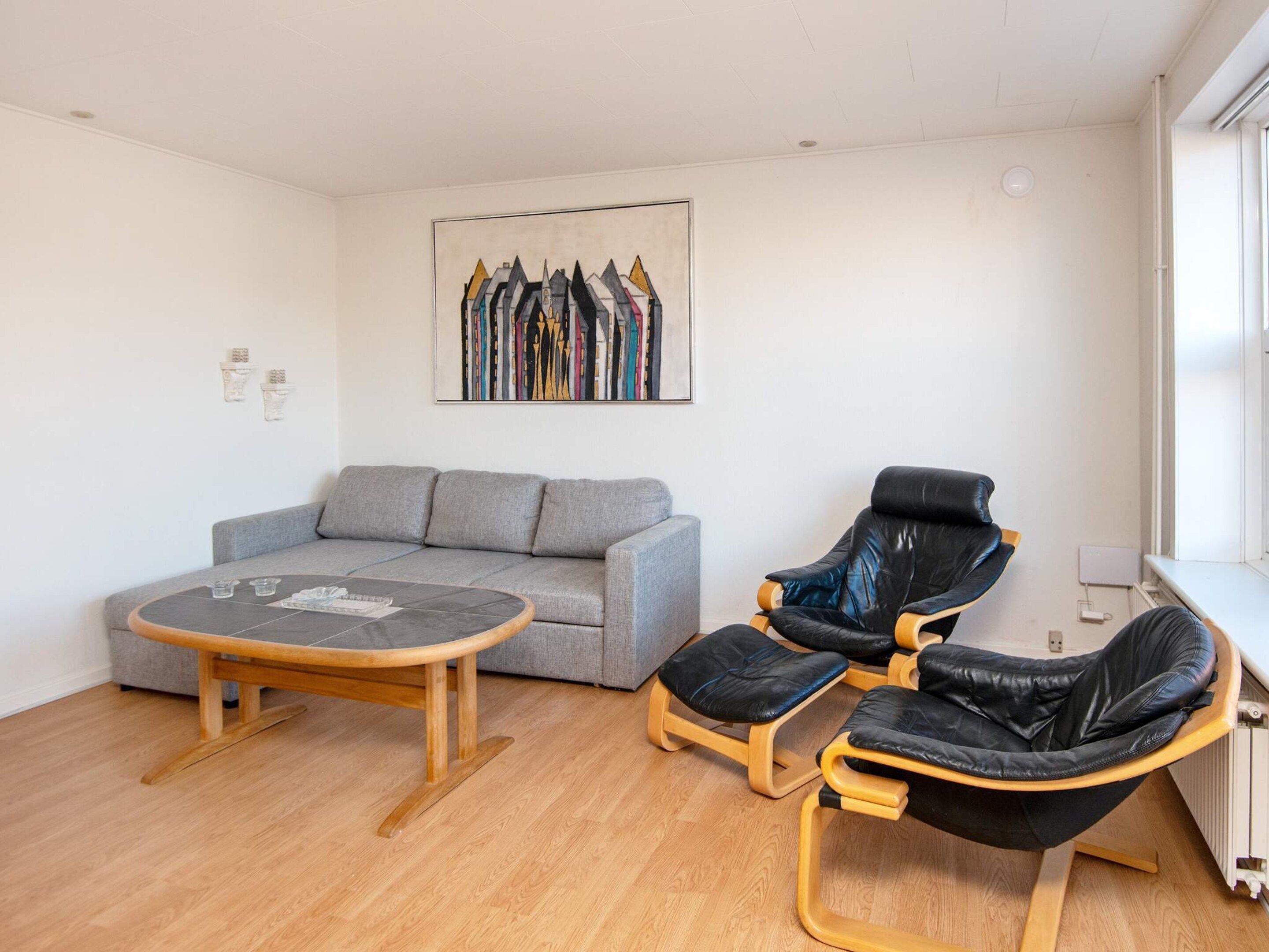 A room with a grey sofa, a wooden coffee table, and two black leather chairs.