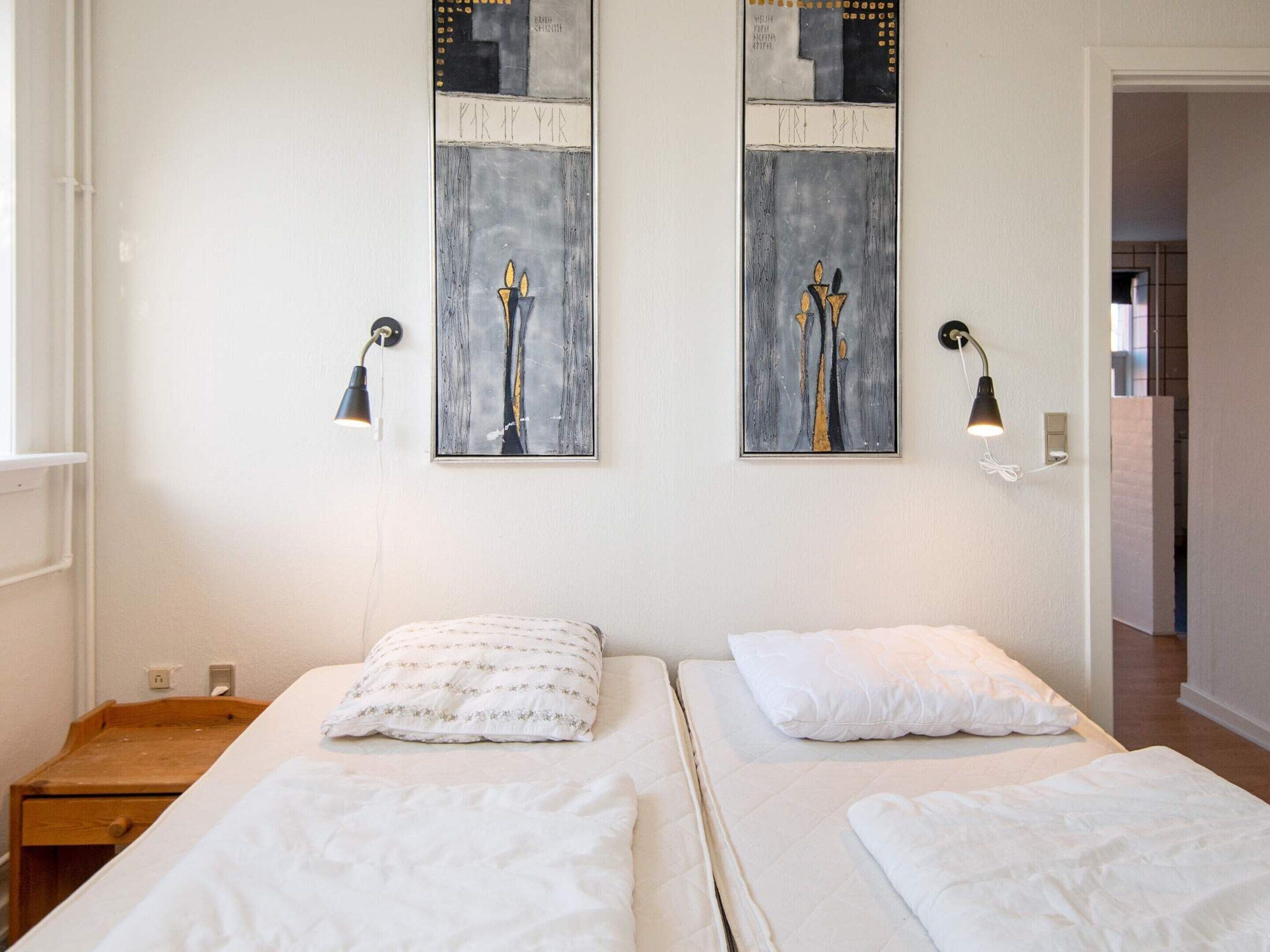 A hotel room with two beds, a wooden nightstand, a wall-mounted lamp, and a framed abstract painting.