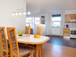 A modern kitchen with a dining area, wooden chairs, a table, and a hanging light fixture.