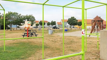 A playground with green metal frames, a picnic table, and a wooden play structure.