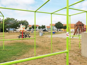 A playground with green metal frames, a picnic table, and a wooden play structure.
