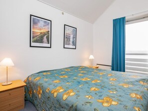 A hotel room with a bed, two framed pictures on the wall, a nightstand with a lamp, and a window with curtains. - 6 Person Holiday Home in Rudkobing (Rudkobing)