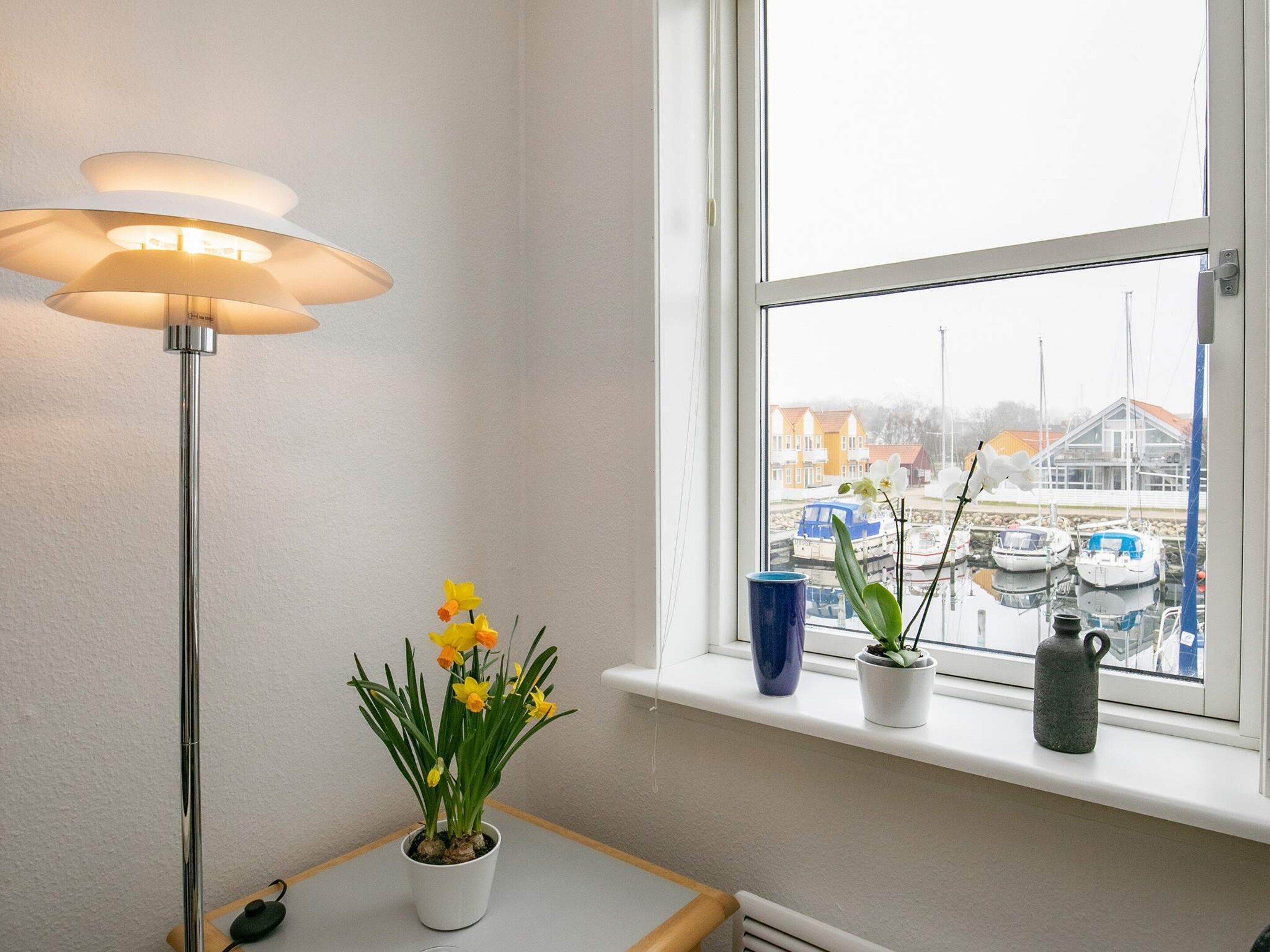 A room with a window, a floor lamp, and a potted plant with yellow flowers.