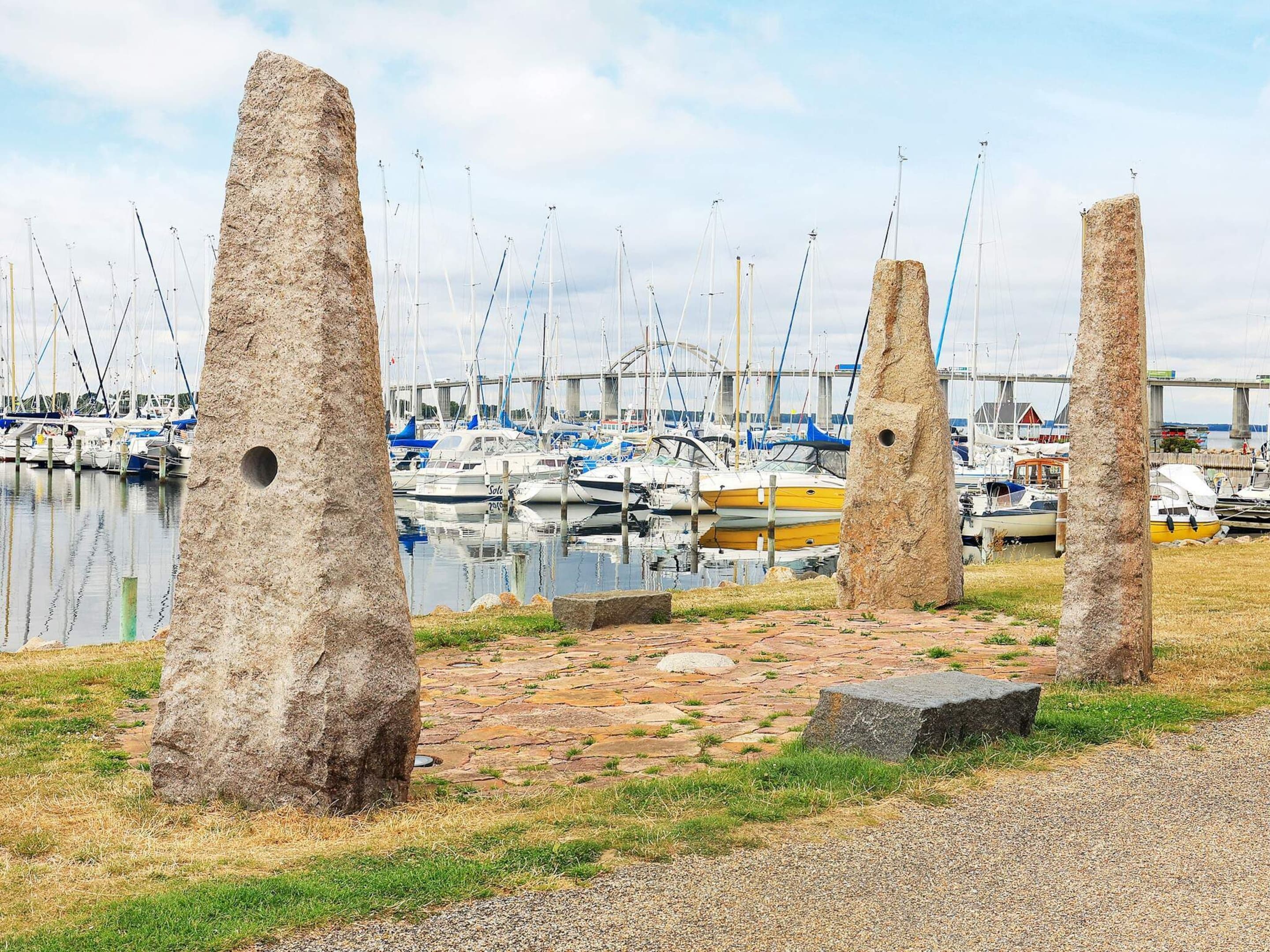 A marina with boats docked, stone pillars, and a bridge in the background.