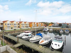 A marina with several boats docked, a wooden dock, and a row of yellow houses with red roofs. - 6 Person Holiday Home in Rudkobing (Rudkobing)