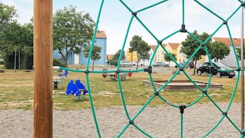 A playground with a rope climbing structure, a blue swing set, and a gravel area.