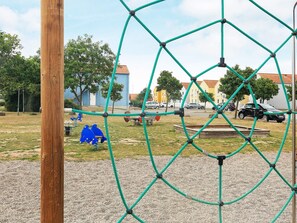 Un parque infantil con una estructura de cuerdas, columpios azules y una zona de grava.
