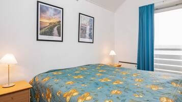 A hotel room with a bed, two bedside lamps, a window with curtains, and two framed pictures on the wall.