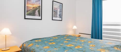 A hotel room with a bed, two bedside lamps, a window with curtains, and two framed pictures on the wall.