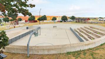 A basketball court with a wooden bench, a metal fence, and a playground in the background.