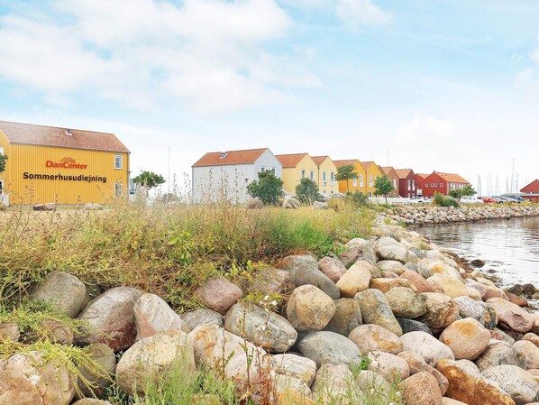 A coastal area with a row of colorful houses, a large yellow building with 'DanCenter' signage, and a rocky shoreline. - 6 Person Holiday Home in Rudkobing (Rudkobing)
