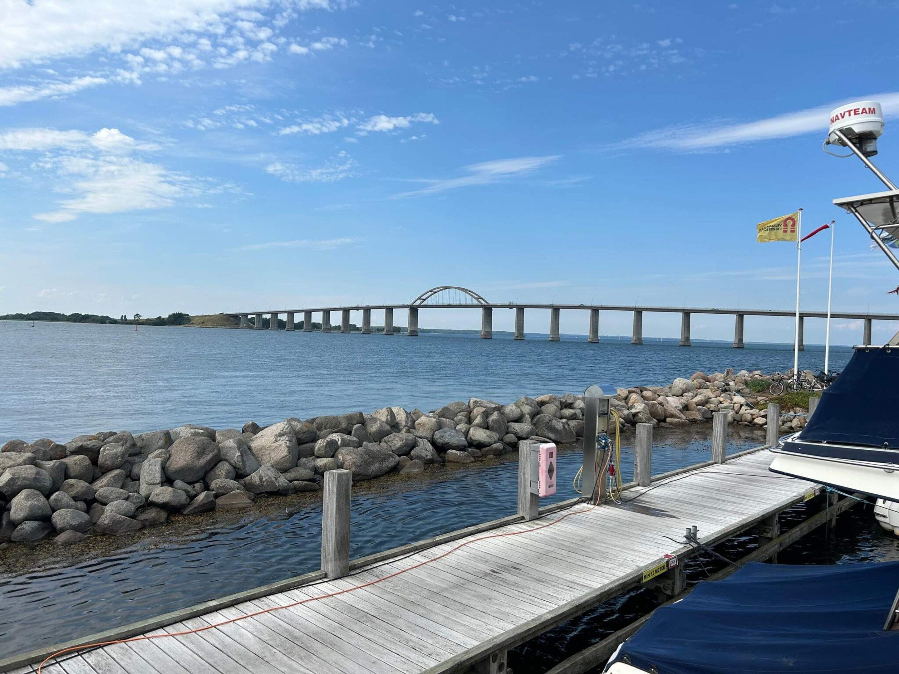A wooden dock extending into calm water with a large bridge in the background.