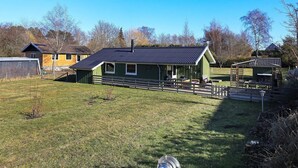 A green building with a sloped roof and a fenced yard. - 6 Person Holiday Home in Humble (Sydlangeland)