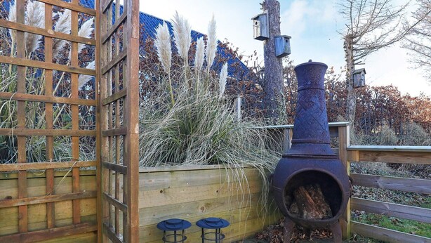 A wooden deck with a rustic outdoor cooking stove, two lanterns, and a wooden fence. - 6 Person Holiday Home in Humble (Sydlangeland)