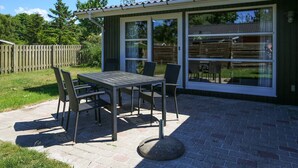 An outdoor patio with a table and chairs, a covered area with sliding glass doors, and a wooden fence in the background. - 4 Person Holiday Home in Store Fuglede (Store Fuglede)