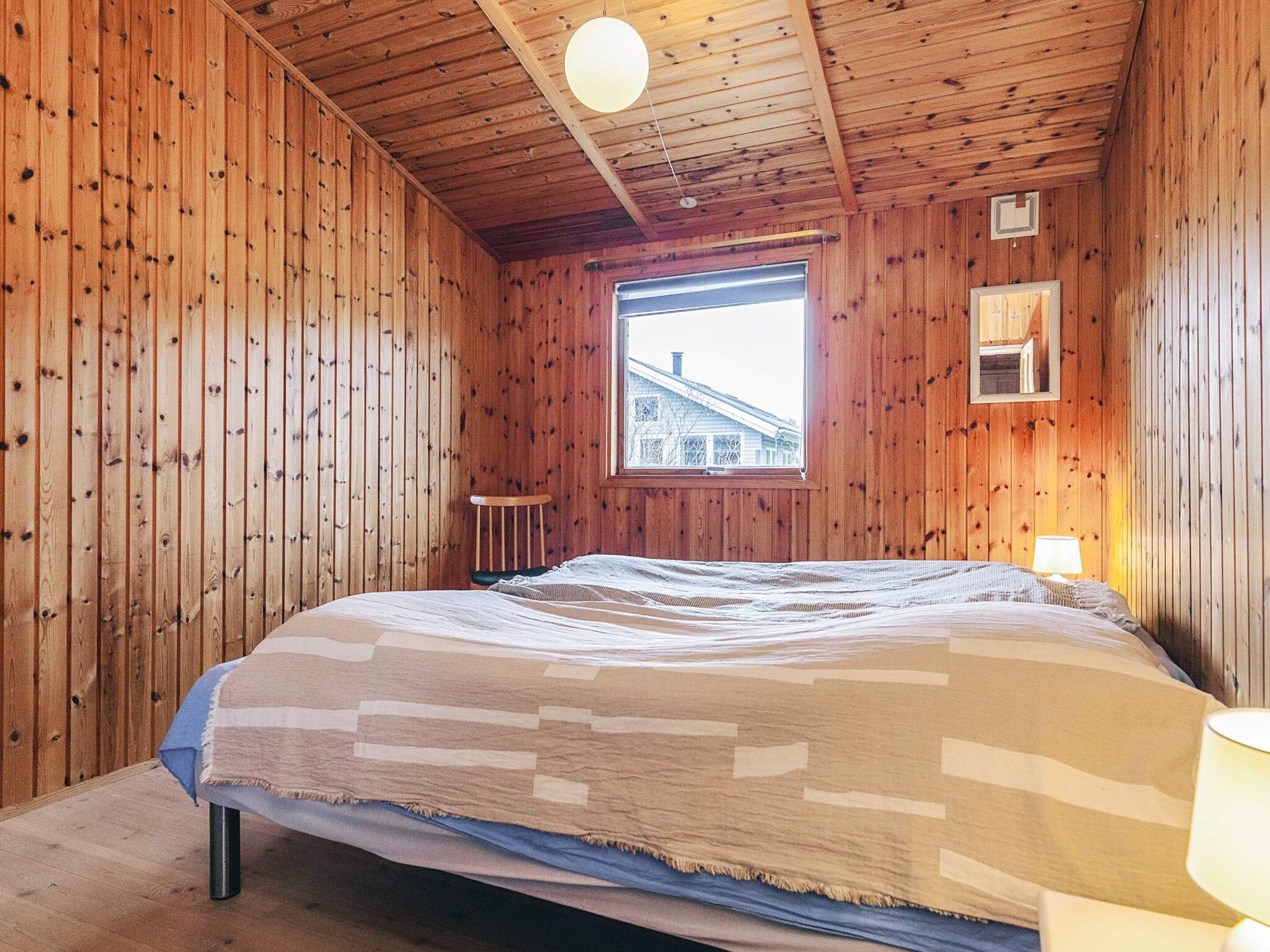 A wooden-paneled room with a bed, a window, and a small table.