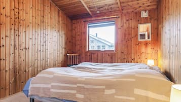 A wooden-paneled room with a bed, a window, and a small table.