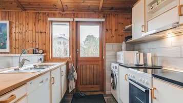 A compact kitchen with wooden walls, a sink, a stove, and a washing machine.
