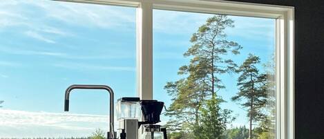 A kitchen with a coffee maker, a bottle, and a window with a view of trees.