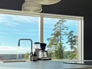 A kitchen with a coffee maker, a bottle, and a window with a view of trees. - 5 Star Holiday Home in Hacksvik (Håcksvik)