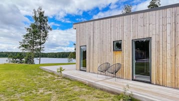 A modern wooden building with a deck, two chairs, and a view of a lake.