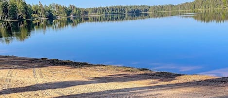 A calm lake with a forested shoreline and a clear sky.