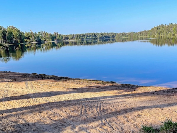 A calm lake with a forested shoreline and a clear sky. - 5 Star Holiday Home in Hacksvik (Håcksvik)