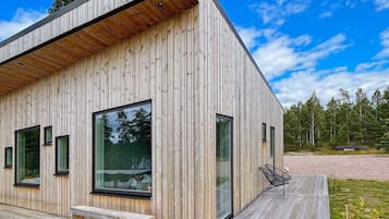 A modern wooden building with large windows, a deck, and a bench.