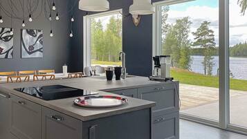 A modern kitchen with a large island, a coffee maker, and a view of a lake through large windows.