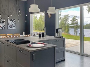 A modern kitchen with a large island, a coffee maker, and a view of a lake through large windows. - 5 Star Holiday Home in Hacksvik (Håcksvik)