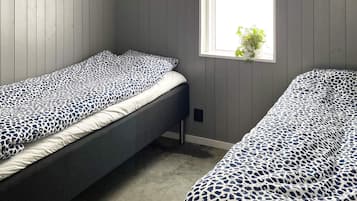 A room with two single beds, each with a leopard print bedspread, a window with a plant, and wooden paneling on the walls.
