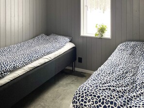 A room with two single beds, each with a leopard print bedspread, a window with a plant, and wooden paneling on the walls. - 5 Star Holiday Home in Hacksvik (Håcksvik)