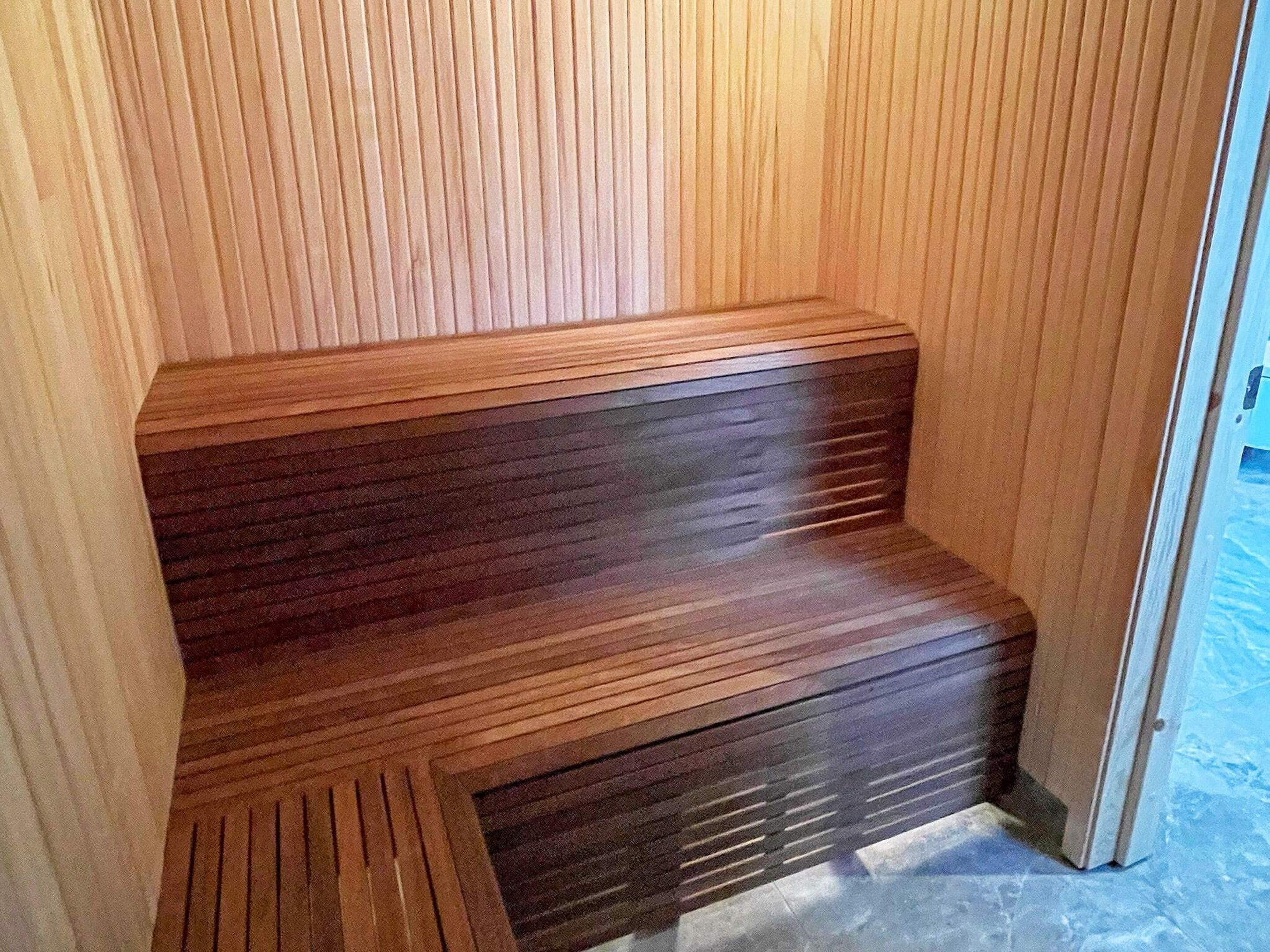 A wooden bench with a slatted design, positioned against a wall with vertical wooden panels.