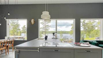 Una cocina moderna con una isla grande, dos ventanas con vista al lago y un techo con vigas a la vista.