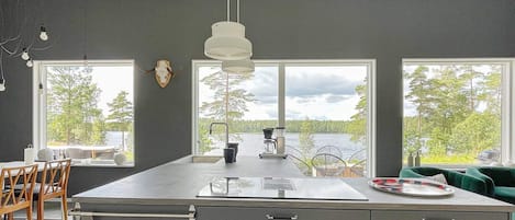 A modern kitchen with a large island, two windows with a lake view, and a ceiling with exposed beams.