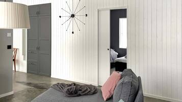 Una sala moderna con un sofá gris, un reloj de pared único y una puerta que da a un dormitorio.