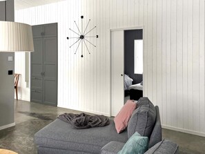 A modern living room with a grey sofa, a unique wall clock, and a door leading to a bedroom. - 5 Star Holiday Home in Hacksvik (Håcksvik)